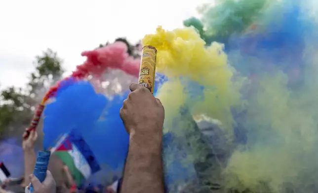 Protesters release smoke in the colors of the Olympic rings during a demonstration by several associations for what they called the "Counter Opening Ceremony" on Republique plaza against the 2024 Summer Olympics, Thursday, July 25, 2024, in Paris. Demonstrators gave speeches about the cost of the Olympic Games and said authorities have been using the Games as a pretext for what they call social cleansing, by removing migrants and homeless people off the streets in order to preserve a picture-postcard image of the city for the millions of visitors coming. (AP Photo/David Goldman)