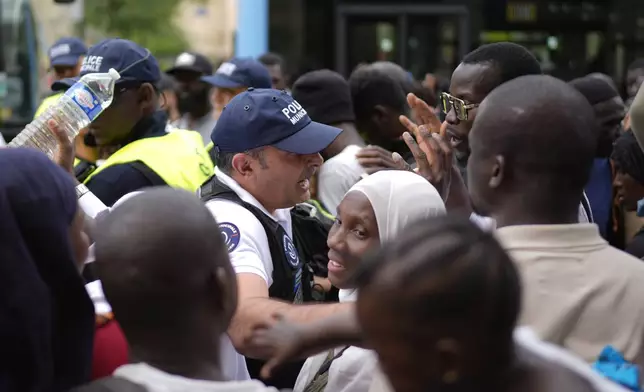 City officials try to maintain calm during a migrants' protest at the 2024 Summer Olympics, Thursday, July 25, 2024, in Paris, France. On the eve of the grandiose opening ceremony for the Paris Olympics, police cleared out migrants sleeping in a tent camp in the capital as social and environmental advocacy groups raise attention to criticisms of the Paris Games such as the displacement of migrants and housing issues. (AP Photo/David Goldman)