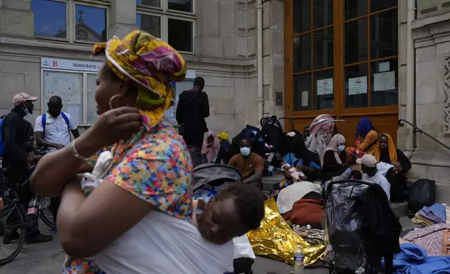 Natasha Louise Gbetie, from Burkina Faso, wihth her son Richard Emmanuel on her back, attend a protest at the 2024 Summer Olympics, Thursday, July 25, 2024, in Paris, France. On the eve of the grandiose opening ceremony for the Paris Olympics, police cleared out migrants sleeping in a tent camp in the capital as social and environmental advocacy groups raise attention to criticisms of the Paris Games such as the displacement of migrants and housing issues. (AP Photo/David Goldman)