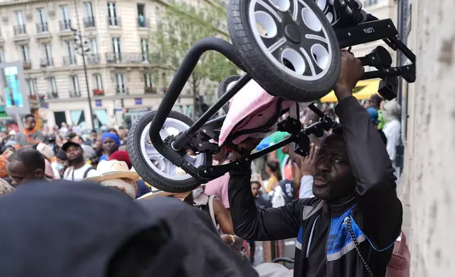 A man passes his stroller over the crowd during a migrants' protest at the 2024 Summer Olympics, Thursday, July 25, 2024, in Paris, France. On the eve of the grandiose opening ceremony for the Paris Olympics, police cleared out migrants sleeping in a tent camp in the capital as social and environmental advocacy groups raise attention to criticisms of the Paris Games such as the displacement of migrants and housing issues. (AP Photo/David Goldman)