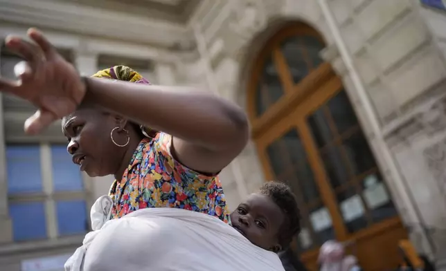 Natasha Louise Gbetie, from Burkina Faso, and her son Richard Emmanuel, attend a protest at the 2024 Summer Olympics, Thursday, July 25, 2024, in Paris, France. On the eve of the grandiose opening ceremony for the Paris Olympics, police cleared out migrants sleeping in a tent camp in the capital as social and environmental advocacy groups raise attention to criticisms of the Paris Games such as the displacement of migrants and housing issues. (AP Photo/David Goldman)