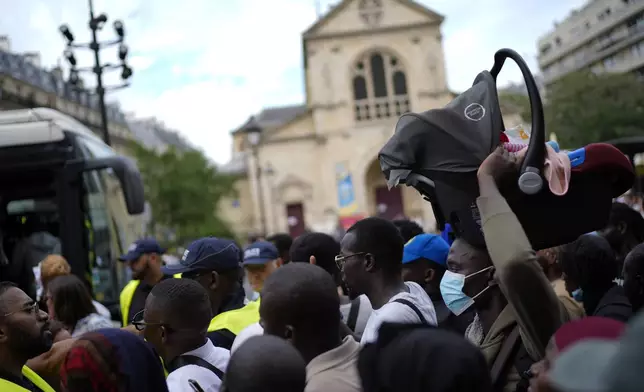 A man carries a baby carrier before boarding a police after a migrants' protest at the 2024 Summer Olympics, Thursday, July 25, 2024, in Paris, France. On the eve of the grandiose opening ceremony for the Paris Olympics, police cleared out migrants sleeping in a tent camp in the capital as social and environmental advocacy groups raise attention to criticisms of the Paris Games such as the displacement of migrants and housing issues. (AP Photo/David Goldman)