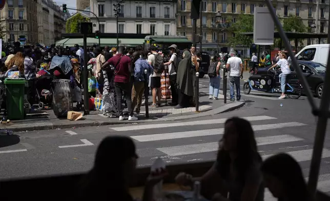 People watch a migrants' protest at the 2024 Summer Olympics, Thursday, July 25, 2024, in Paris, France. On the eve of the grandiose opening ceremony for the Paris Olympics, police cleared out migrants sleeping in a tent camp in the capital as social and environmental advocacy groups raise attention to criticisms of the Paris Games such as the displacement of migrants and housing issues. (AP Photo/David Goldman)