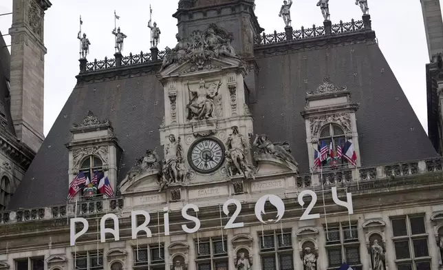 The logo of the Paris 2024 Olympic Games hangs from the facade of the Paris city hall, Wednesday, July 3, 2024 in Paris. Just three weeks before the Olympics, the excitement that was building up in the host city has mingled with anxiety about France’s political future. (AP Photo/Thibault Camus)