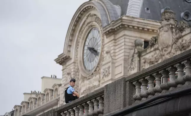 A police officer stands watch near the Musée d'Orsay as the city prepares for the start of the opening ceremony in Paris, France, before the the 2024 Summer Olympics, Friday, July 26, 2024. (AP Photo/Rebecca Blackwell)