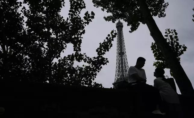 A couple waits for the opening ceremony of the 2024 Summer Olympics to begin in front of the Eiffel Tower, Friday, July 26, 2024, in Paris, France. (AP Photo/Alessandra Tarantino)