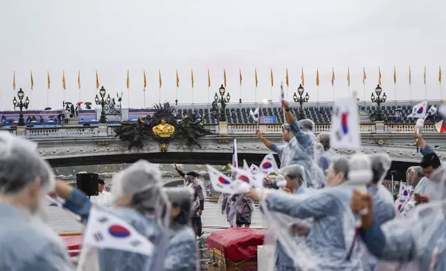 Team South Korea, wearing rain coats, wave their flag from a boat in Paris, France, during the opening ceremony of the 2024 Summer Olympics, Friday, July 26, 2024. (AP Photo/Lee Jin-man, Pool)