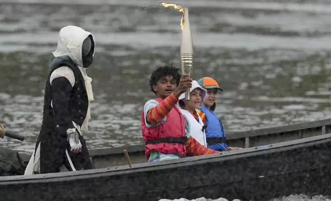 A torch is carried in Paris, France, during the opening ceremony of the 2024 Summer Olympics, Friday, July 26, 2024. (AP Photo/Kin Cheung)