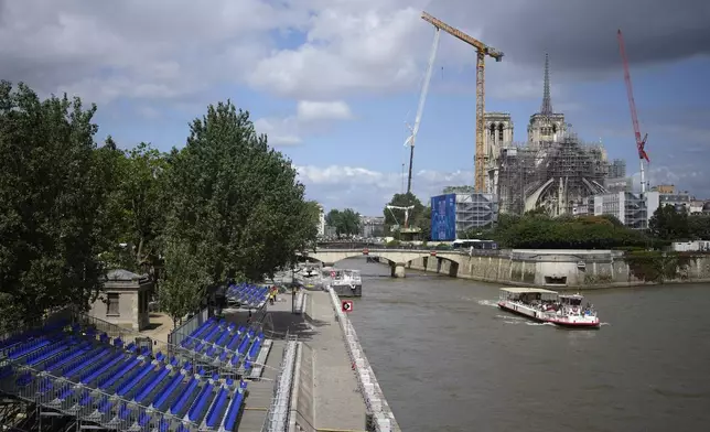 A tourists boat makes its way on the Seine river with stands installed on its banks, Thursday, July 4, 2024 by Notre Dame de Pari cathedral in Paris. The Seine river will host the Paris Olympic Games opening ceremony on July 26. (AP Photo/Thibault Camus)