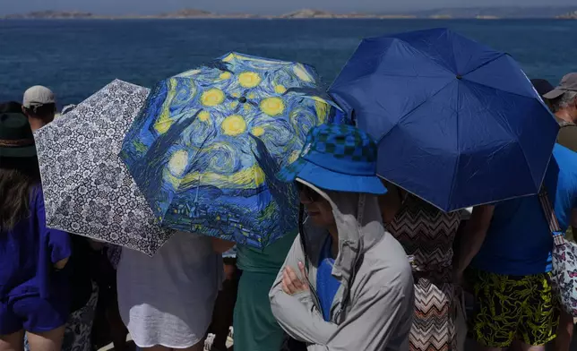 Fans use umbrella to shelter from the sun as they line the shore at the Olympic marina to see sailing boats come and go, during the 2024 Summer Olympics, Monday, July 29, 2024, in Marseille, France. (AP Photo/Carolyn Kaster)