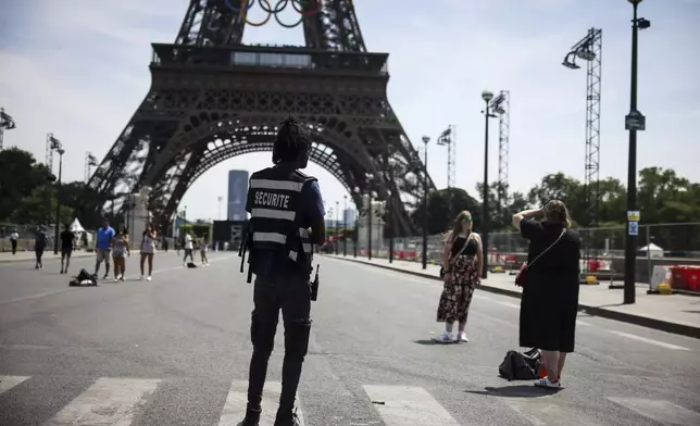 A security officer watches people taken photographs in front of the Eiffel Tower at the 2024 Summer Olympics, Saturday, July 20, 2024, in Paris, France. (AP Photo/Thomas Padilla)