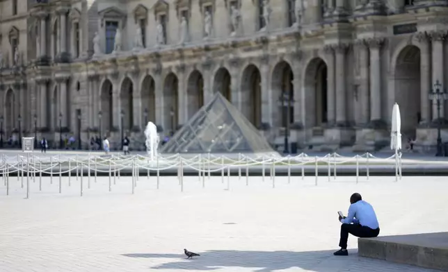 A lone man sit in the shadow in the courtyard of the Louvre museum, which is outside the security perimeter set up for the Olympic Games, Friday, July 19, 2024, in Paris, France. (AP Photo/David Goldman)