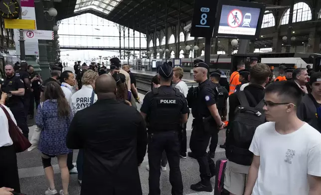 Travelers wait as police officers patrol inside the Gare du Nord train station at the 2024 Summer Olympics, Friday, July 26, 2024, in Paris, France. Hours away from the grand opening ceremony of the Olympics, high-speed rail traffic to the French capital was severely disrupted on Friday by what officials described as "criminal actions" and sabotage. (AP Photo/Mark Baker)