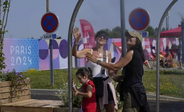 A family cools themselves under water spraying fans as the temperature rises at the 2024 Summer Olympics shooting venue in Chateauroux, France, Monday, July 29, 2024. (AP Photo/Manish Swarup)