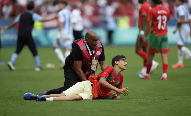 A steward catches a pitch invader during the men's Group B soccer match between Argentina and Morocco at Geoffroy-Guichard Stadium at the 2024 Summer Olympics, Wednesday, July 24, 2024, in Saint-Etienne, France. (AP Photo/Silvia Izquierdo)