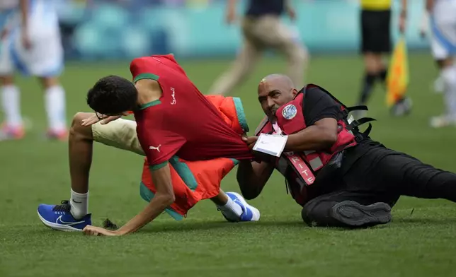 A steward catches a pitch invader during the men's Group B soccer match between Argentina and Morocco at Geoffroy-Guichard Stadium at the 2024 Summer Olympics, Wednesday, July 24, 2024, in Saint-Etienne, France. (AP Photo/Silvia Izquierdo)