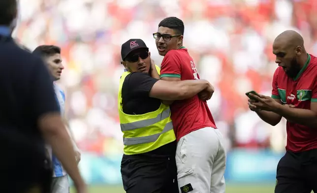 A steward catches a pitch invader during the men's Group B soccer match between Argentina and Morocco at Geoffroy-Guichard Stadium at the 2024 Summer Olympics, Wednesday, July 24, 2024, in Saint-Etienne, France. (AP Photo/Silvia Izquierdo)