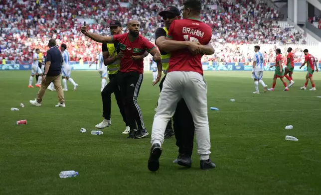 Stewards catch pitch invaders during the men's Group B soccer match between Argentina and Morocco at Geoffroy-Guichard Stadium at the 2024 Summer Olympics, Wednesday, July 24, 2024, in Saint-Etienne, France. (AP Photo/Silvia Izquierdo)