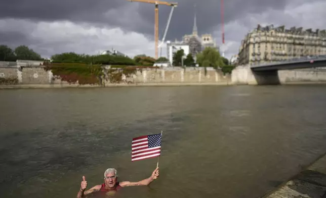Joel Stratte-McClure, 75, of the US, holds American flag after completing a short swim in the Seine river, Thursday, July 4, 2024 in Paris. The Seine River has been found unsafe according to test results published last Friday, less than a month before the Paris Olympics. (AP Photo/Thibault Camus)