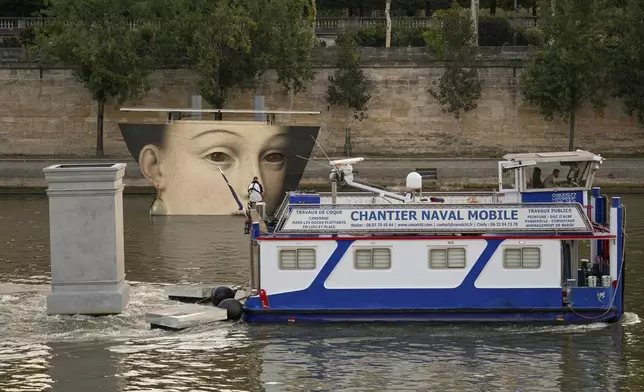 A ship sails past reproductions of artworks decorating the banks of the River Seineat the 2024 Summer Olympics, Tuesday, July 30, 2024, in Paris, France. The men's Olympic triathlon has been postponed over concerns about water quality in Paris' Seine River, where the swimming portion of the race was supposed to take place. (AP Photo/Vadim Ghirda)