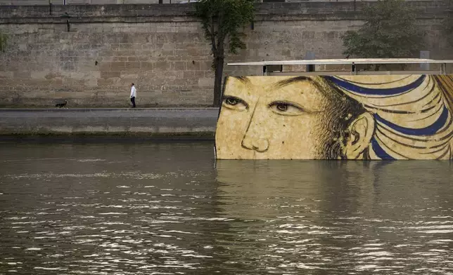 A man walks with a dog past reproductions of artworks decorating the banks of the River Seineat the 2024 Summer Olympics, Tuesday, July 30, 2024, in Paris, France. The men's Olympic triathlon has been postponed over concerns about water quality in Paris' Seine River, where the swimming portion of the race was supposed to take place. (AP Photo/ Dar Yasin)