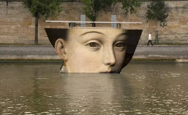 A man wipes his face as he walks past reproductions of artworks decorating the banks of the River Seineat the 2024 Summer Olympics, Tuesday, July 30, 2024, in Paris, France. The men's Olympic triathlon has been postponed over concerns about water quality in Paris' Seine River, where the swimming portion of the race was supposed to take place. (AP Photo/Vadim Ghirda)