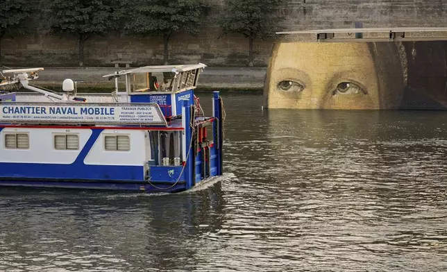 A ship sails past reproductions of artworks decorating the banks of the River Seineat the 2024 Summer Olympics, Tuesday, July 30, 2024, in Paris, France. The men's Olympic triathlon has been postponed over concerns about water quality in Paris' Seine River, where the swimming portion of the race was supposed to take place. (AP Photo/ Dar Yasin)