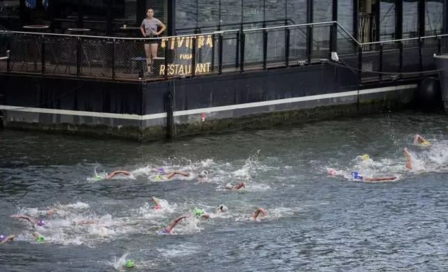 A woman watches athletes competing during the swim leg of the women's individual triathlon competition at the 2024 Summer Olympics, Wednesday, July 31, 2024, in Paris, France. (AP Photo/Dar Yasin)