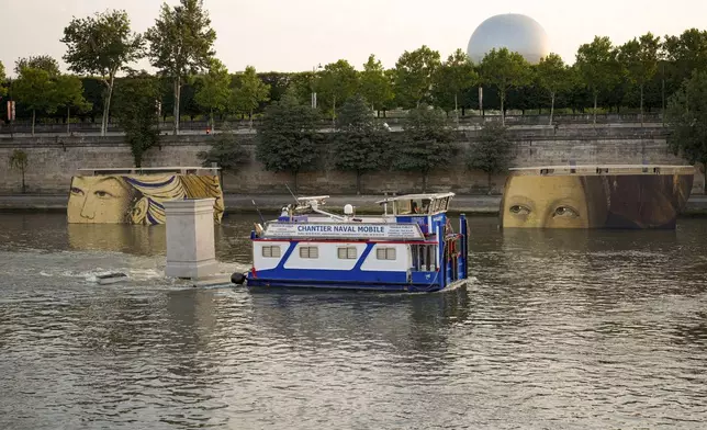 A boat sails past reproductions of artworks decorating the banks of the River Seineat the 2024 Summer Olympics, Tuesday, July 30, 2024, in Paris, France. The men's Olympic triathlon has been postponed over concerns about water quality in Paris' Seine River, where the swimming portion of the race was supposed to take place. (AP Photo/ Dar Yasin)