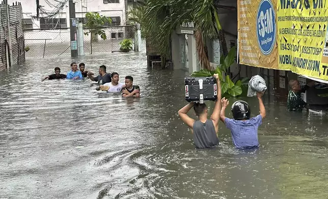 People wade through a flooded street following monsoon rains worsened by offshore typhoon Gaemi on Wednesday, July 24, 2024, in Manila, Philippines. (AP Photo/Joeal Capulitan)