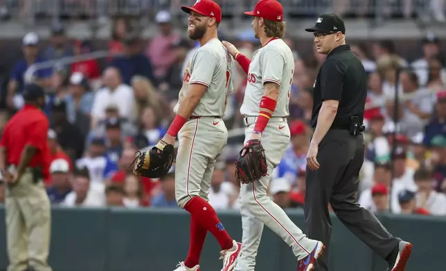 Philadelphia Phillies first baseman Kody Clemens, left, is checked on by second baseman Bryson Stott, center, after a collision with Atlanta Braves' Jarred Kelenic, not pictured, in the third inning of a baseball game against the Atlanta Braves, Saturday, July 6, 2024, in Atlanta. (AP Photo/Brett Davis)