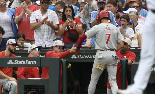 Philadelphia Phillies' Trea Turner (7) celebrates with manager Rob Thomson, third from left, at the dugout after scoring on a Brandon Marsh single during the first inning of a baseball game against the Chicago Cubs, Thursday, July 4, 2024, in Chicago. (AP Photo/Paul Beaty)