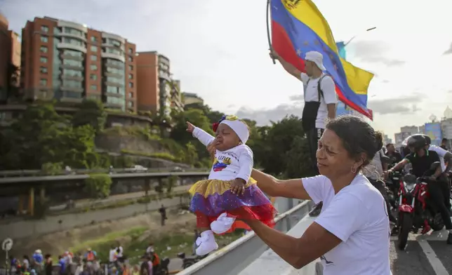 A supporter of opposition presidential candidate Edmundo Gonzalez holds a baby over a highway overpass, waiting for him and opposition leader Maria Corina Machado to pass by during their closing election campaign rally in Caracas, Venezuela, Thursday, July 25, 2024. The presidential election is set for July 28. (AP Photo/Cristian Hernandez)