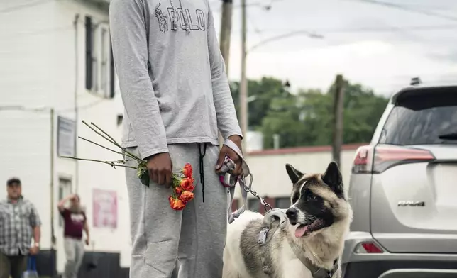 A man holds flowers while standing with his dog during a vigil for 13-year-old Nyah Mway in Utica, N.Y., Saturday, June 29, 2024. On Friday, June 28, Mway was fatally shot by police who’d tackled him to the ground after he allegedly pointed what turned out to be a BB gun at them during a foot chase. (Daniel DeLoach/Observer-Dispatch via AP)