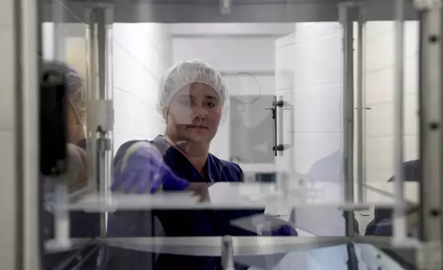 A worker at United Therapeutics' designated pathogen-free facility in Christiansburg, Va., on May 29, 2024 retrives a UV sterilized item from behind a protected barrier within the facility. (AP Photo/Shelby Lum)