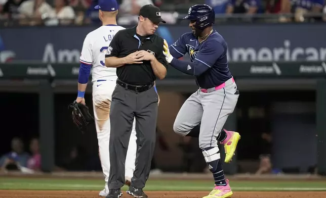 Tampa Bay Rays' Yandy Diaz, right, runs into umpire Junior Valentine, front left, while rounding the bases past Texas Rangers first baseman Nathaniel Lowe, back left, after hitting a three-run home run in the seventh inning of a baseball game in Arlington, Texas, Saturday, July 6, 2024. (AP Photo/Tony Gutierrez)