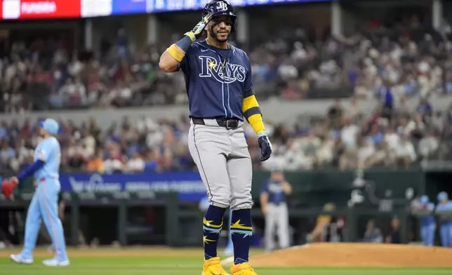 Tampa Bay Rays' Jose Caballero, foreground, salutes the dugout as he rounds the bases after hitting a two-run home run off Texas Rangers' Nathan Eovaldi, back left, in the third inning of a baseball game in Arlington, Texas, Sunday, July 7, 2024. (AP Photo/Tony Gutierrez)