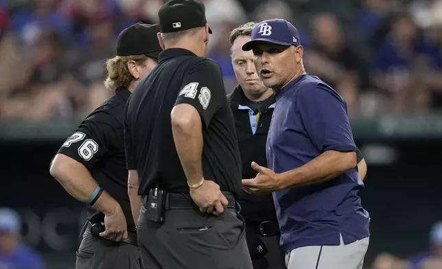 Tampa Bay Rays manager Kevin Cash, right, talks with umpires Andy Fletcher (49) and Mike Muchlinksi (76) after Randy Arozarena was called out in an at-bat due to fan interference in the seventh inning of a baseball game against the Texas Rangers in Arlington, Texas, Sunday, July 7, 2024. The call was upheld after a video review. (AP Photo/Tony Gutierrez)