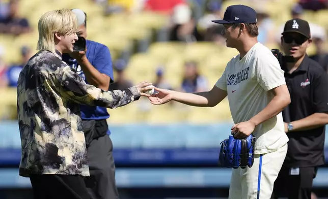 DJ Matsunaga, left, of the band Creepy Nuts, gets a ball from Los Angeles Dodgers pitcher Yoshinobu Yamamoto, second form right, after throwing a ceremonial first pitch before a baseball game between the Los Angeles Dodgers and the Boston Red Sox, Saturday, July 20, 2024, in Los Angeles. (AP Photo/Marcio Jose Sanchez)