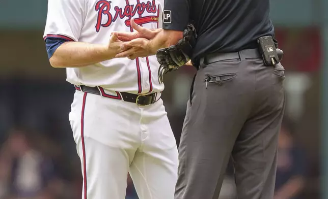 Atlanta Braves pitcher Grant Holmes has his hands and clove checked by the umpire in the third inning of the first baseball game of a against the Cincinnati Reds, Wednesday, July 24, 2024, in Atlanta. (AP Photo/Jason Allen)