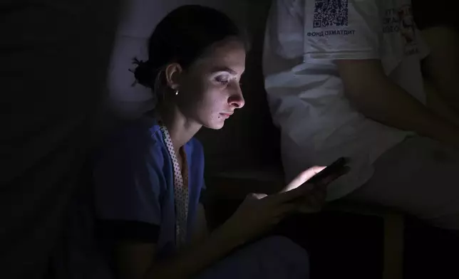 A nurse looks at her phone as she takes shelter in a basement after Russian missile hit the country's main children hospital Okhmadit in Kyiv, Ukraine, Monday, July 8, 2024. The daytime barrage targeted five Ukrainian cities with more than 40 missiles of different types hitting apartment buildings and public infrastructure, President Volodymyr Zelenskyy said on social media. (AP Photo/Anton Shtuka)