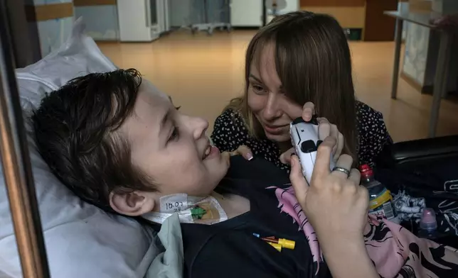 Yuliia Vasylenko smiles with her son Denys, 11, as he plays on a video game console at the National Cancer Institute in Kyiv, Ukraine, Wednesday, July 10, 2024. Denys is one of 31 young patients battling cancer who were relocated to the hospital from Okhmatdyt Children’s Hospital after it was struck by a Russian missile this week. (AP Photo/Alex Babenko)