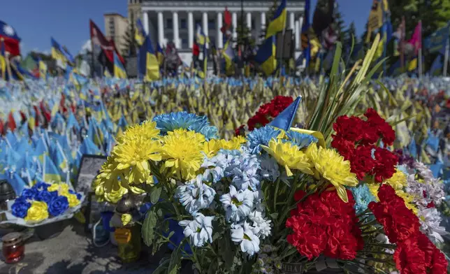 Various flowers are seen in front of a field of flags in memory of fallen fighters, in Kyiv, Ukraine, Tuesday, June 25, 2024. Despite hardships brought by war flowers fill Kyiv and other Ukrainian cities. They burst out of planters that line the capital's backroads and grand boulevards and are fixed to lampposts. (AP Photo/Anton Shtuka)