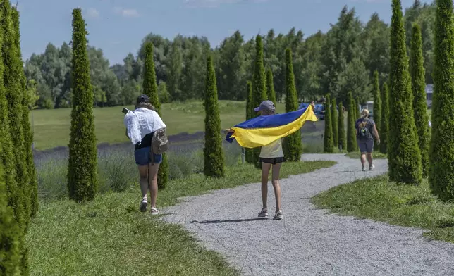 A girl uses a Ukrainian flag to shelter from the sun in Dobro Park, Motyzhyn, Kyiv region, Ukraine, Wednesday, June 26, 2024. Despite hardships brought by war flowers fill Kyiv and other Ukrainian cities. Dobro Park, a 370-acre (150 hectare) privately-run garden and recreation area west of Kyiv, was rebuilt after the Russian attack and occupation that lasted for more than a month.(AP Photo/Anton Shtuka)