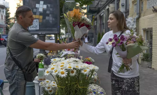A woman buys bouquets of flowers at a street flower stall in Kyiv, Ukraine, Tuesday, June 25, 2024. Despite hardships brought by war flowers fill Kyiv and other Ukrainian cities. They burst out of planters that line the capital's backroads and grand boulevards and are fixed to lampposts. (AP Photo/Anton Shtuka)