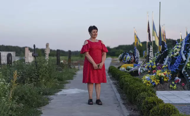 Oksana, the mother of a Ukrainian serviceman who was killed in the 2022 explosions at the Olenivka prison, stands near the grave of her son at a cemetery in Kremenchuk, Donetsk region, Ukraine, Friday, July 12, 2024. An AP investigation interviewed survivors, family and investigators and obtained an internal U.N. analysis. All pointed to Russia as the culprit.(AP Photo/Evgeniy Maloletka)