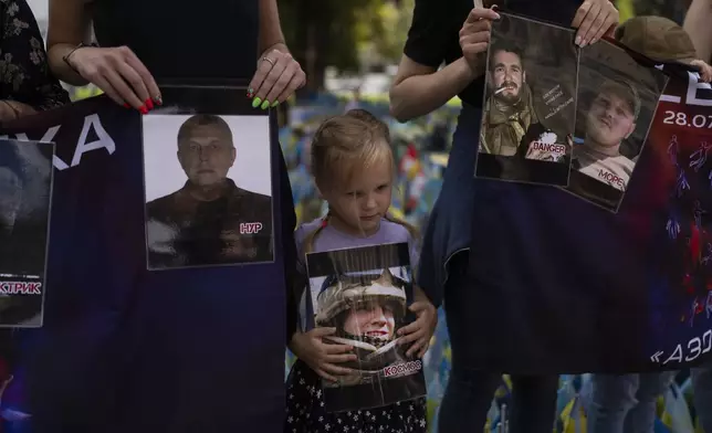 FILE - A girl holds a photo of a Ukrainian POW killed in the 2022 explosions at the Russian-controlled prison barracks in Olenivka, eastern Ukraine, during a memorial in Kyiv on July 29, 2023. An AP investigation interviewed survivors, family and investigators and obtained an internal U.N. analysis. All pointed to Russia as the culprit. (AP Photo/Jae C. Hong, File)