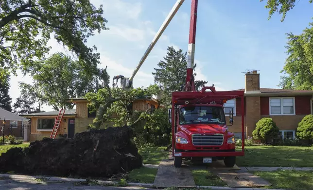 Workers clear a tree that toppled onto a home in Norridge, Illinois, Tuesday, July 16, 2024. The tree was toppled as storms with reports of tornadoes blew through Iowa, Illinois and Indiana. (AP Photo/Teresa Crawford)