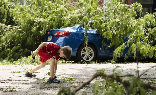 Ezra Solomon, 8, helps clear the road of debris near the intersection of West Huron and North Leavitt streets in Chicago's West Town neighborhood, Tuesday, July 16, 2024, after severe storms passed through the Chicago area the night before. (Pat Nabong/Chicago Sun-Times via AP)