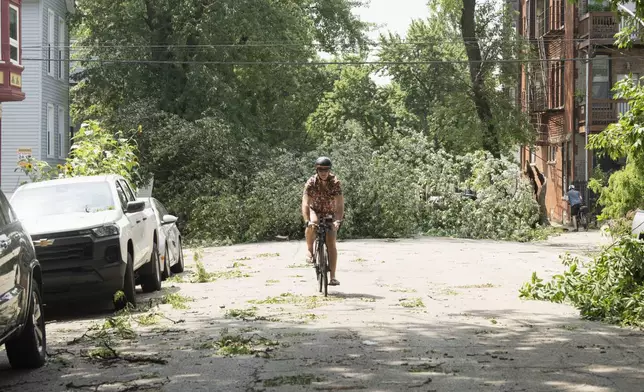 A cyclist rides a bike as a downed tree blocks the road near the intersection of West Huron Street and North Hoyne Avenue in Chicago's West Town neighborhood, Tuesday, July 16, 2024, after severe storms passed through the Chicago area the night before. (Pat Nabong/Chicago Sun-Times via AP)